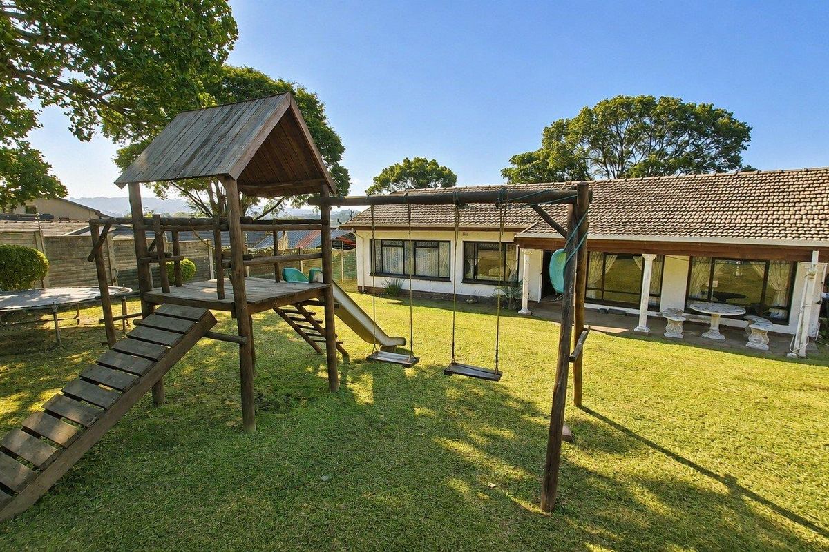 Spacious rear garden featuring a lawn area, a children's play structure, and a covered patio attached to the main house.