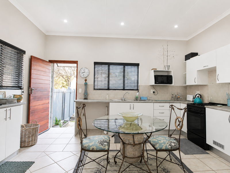 Open-plan kitchen and dining area featuring white cabinetry, tiled flooring, built-in oven, and direct access to the exterior through a timber door.