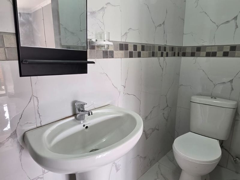 A clean, modern bathroom featuring marble-effect wall tiles, a mosaic border, a pedestal washbasin with chrome fixtures, and a standard ceramic toilet.