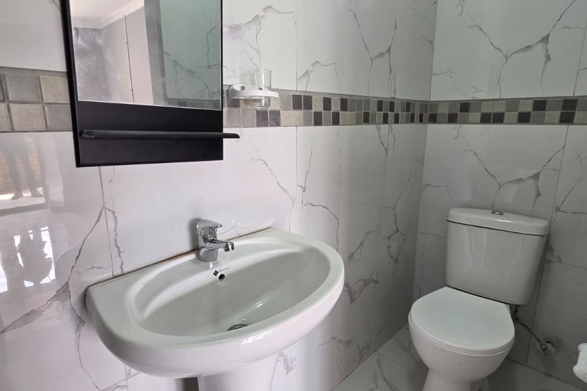 A clean, modern bathroom featuring marble-effect wall tiles, a mosaic border, a pedestal washbasin with chrome fixtures, and a standard ceramic toilet.