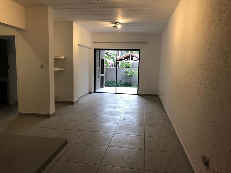 An empty, open-plan living area featuring neutral tiled flooring, textured walls, and a sliding glass door providing access to an outdoor patio space.