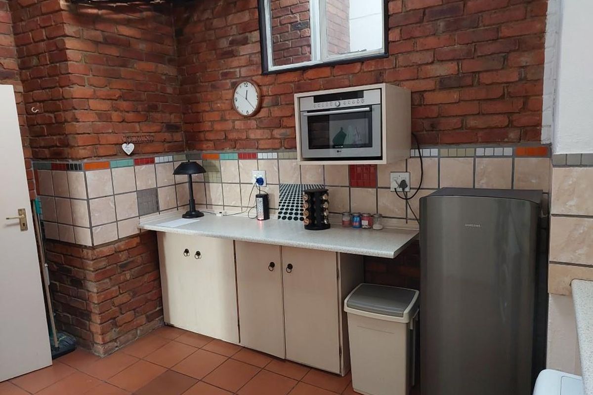A functional kitchen area featuring exposed brick walls, tiled flooring, built-in cabinetry, and a mounted microwave.