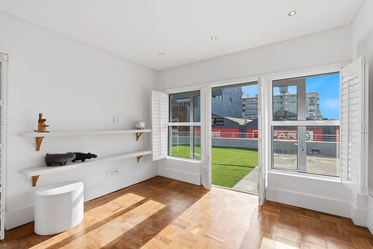 Bright living area featuring polished parquet flooring, built-in shelving, and large glass doors opening onto a private terrace with artificial turf.