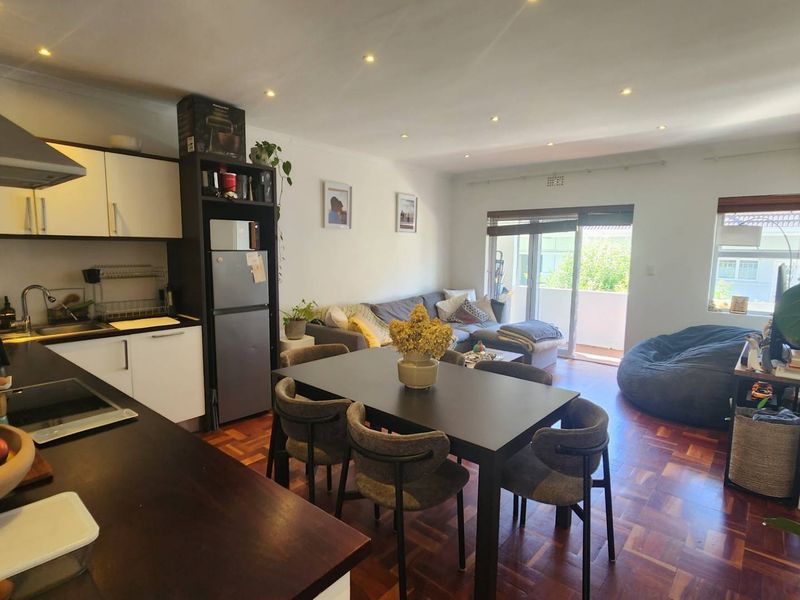 Open-plan living and kitchen area featuring warm parquet flooring, recessed lighting, and direct access to a balcony through sliding glass doors.