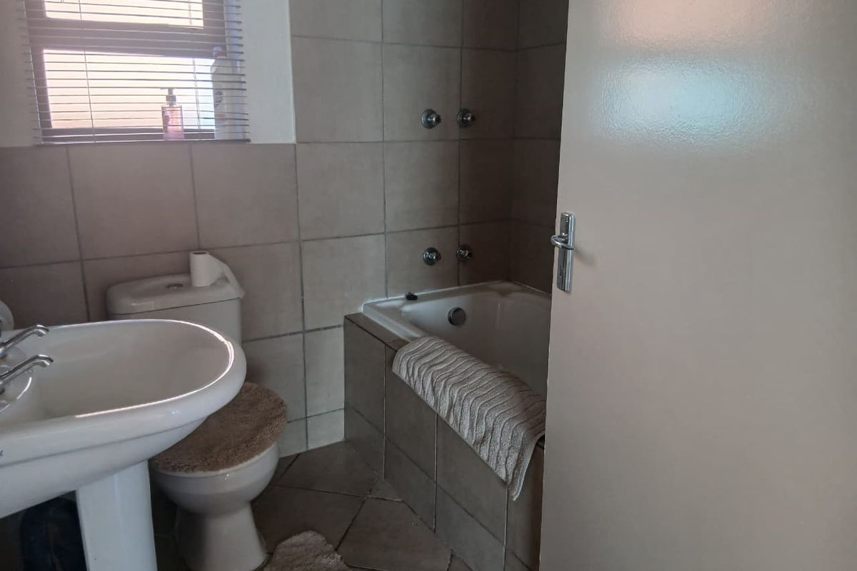 A functional bathroom featuring a pedestal basin, a tiled bathtub with shower mixer, and neutral wall and floor tiling.