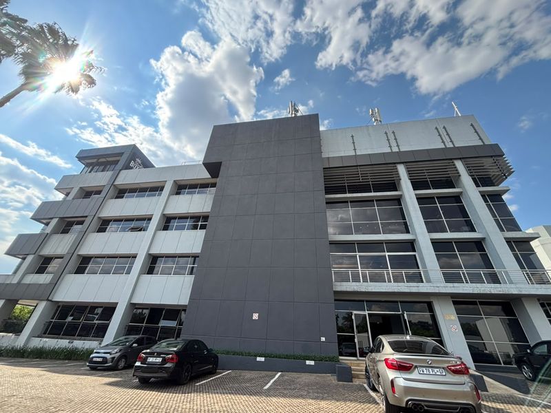 A modern multi-story office building featuring a contemporary glass and panel facade with an integrated ground-level parking area.