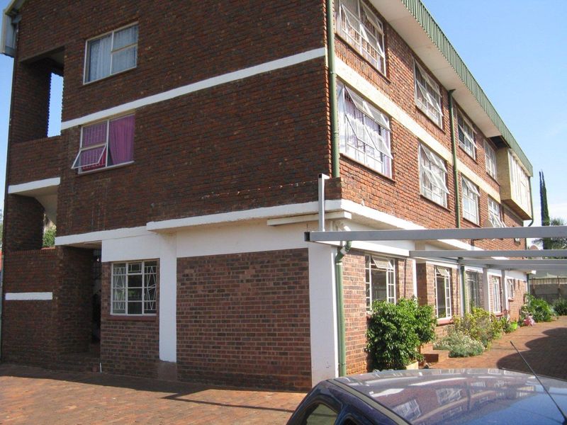 Exterior view of a multi-story face-brick apartment building featuring steel-framed windows and a paved driveway with covered parking bays.