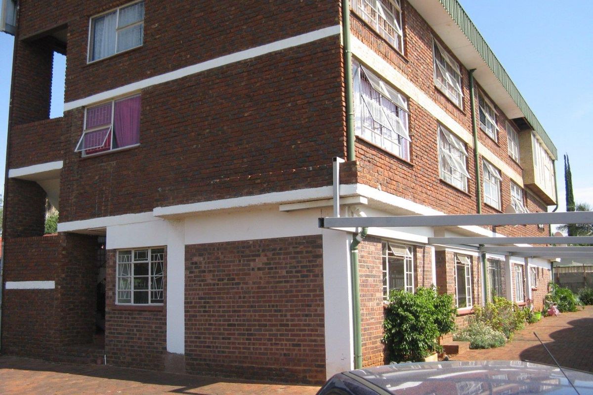 Exterior view of a multi-story face-brick apartment building featuring steel-framed windows and a paved driveway with covered parking bays.