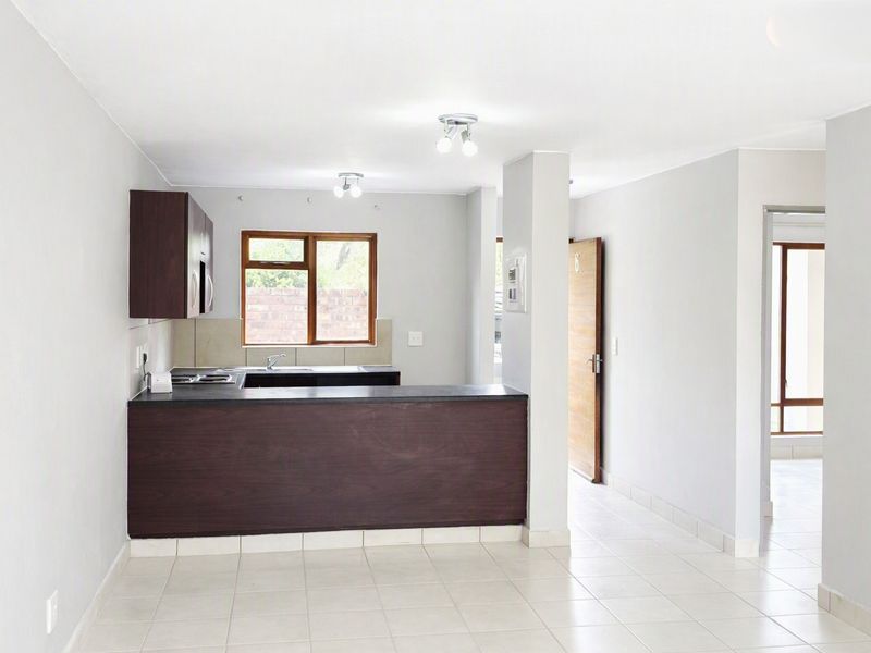 An open-plan kitchen and living area featuring dark wood cabinetry, tiled flooring, and neutral walls, offering a clean and functional space.
