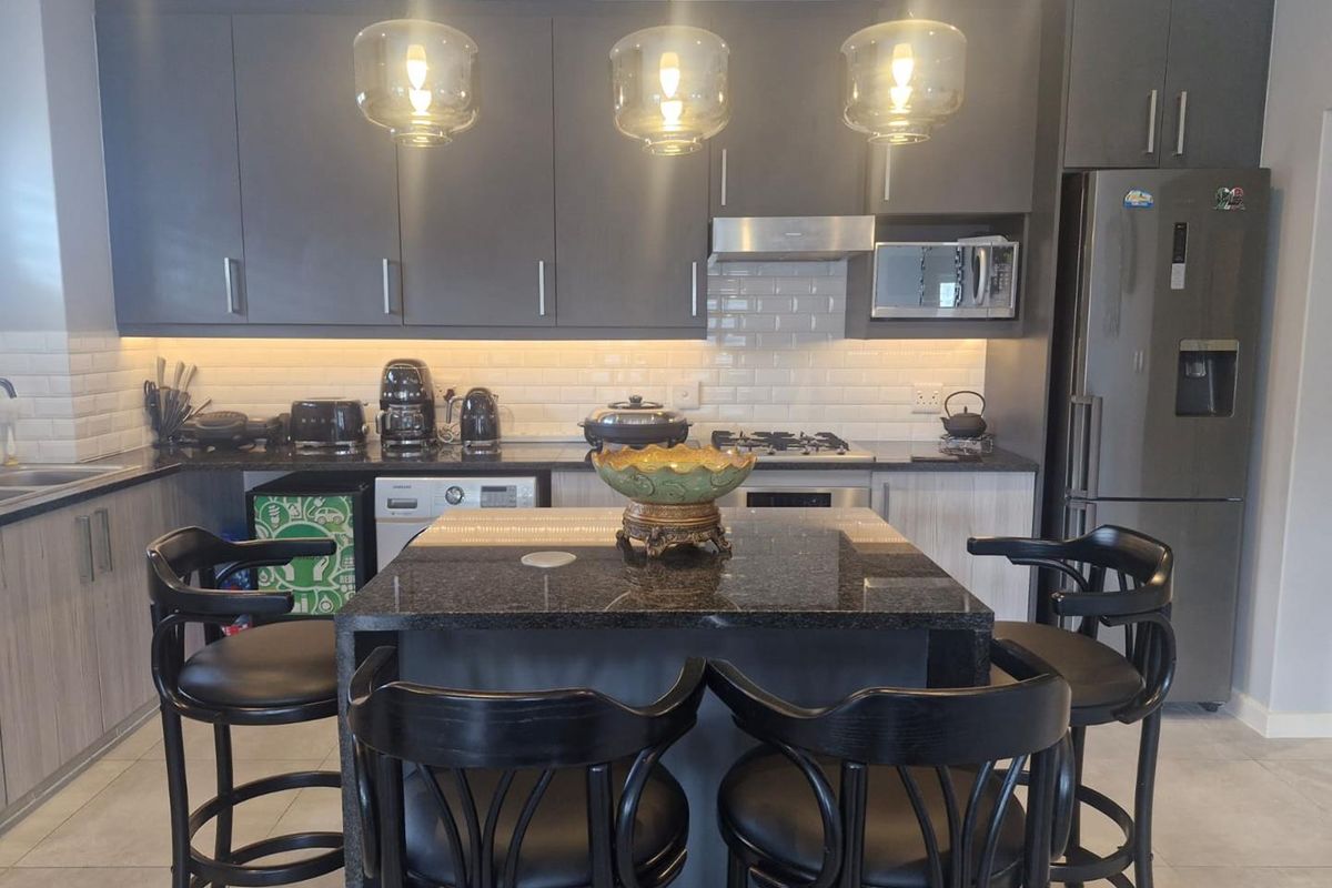Modern kitchen featuring dark cabinetry, granite countertops, a central island with breakfast bar seating, subway tile backsplash, and integrated stainless steel appliances.