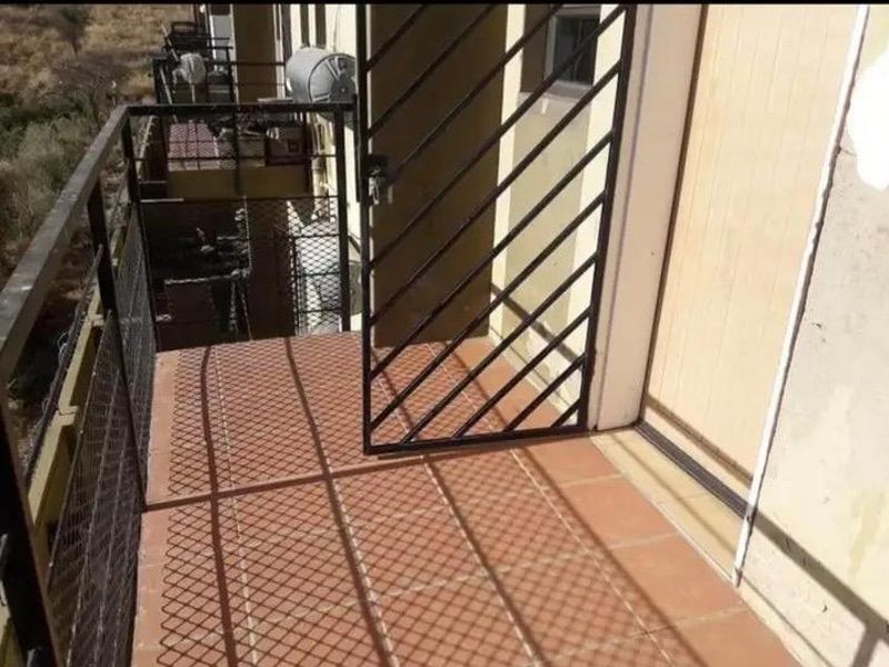 A functional balcony featuring tiled flooring, a metal security gate, and a metal balustrade, providing an outdoor space for the apartment.