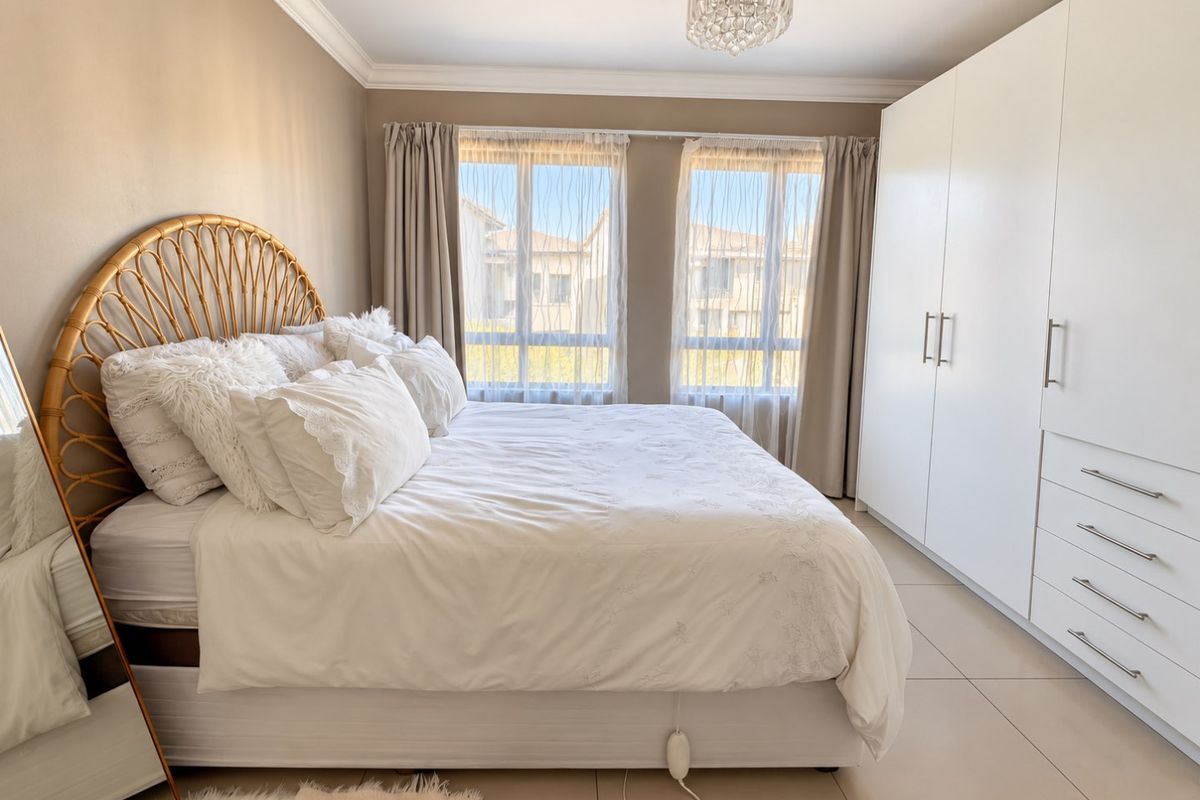 A well-maintained bedroom featuring neutral wall tones, large built-in cupboards, tiled flooring, and elegant crown molding, providing a bright and comfortable living space.