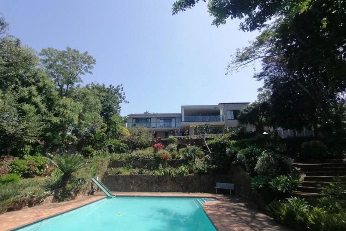 Rear view of the property featuring a swimming pool with a slide, set against a multi-level terraced garden and stone retaining walls.
