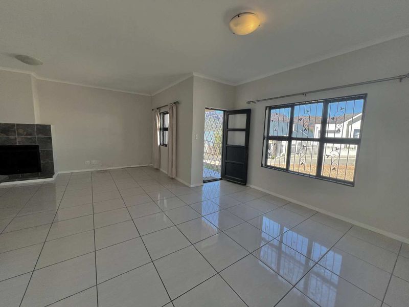 Spacious, light-filled living room featuring neutral tiled flooring, a built-in fireplace, and secure window bars, offering a clean canvas for interior design.