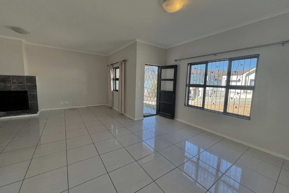 Spacious, light-filled living room featuring neutral tiled flooring, a built-in fireplace, and secure window bars, offering a clean canvas for interior design.