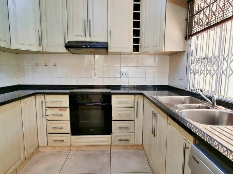 Functional kitchen featuring built-in cabinetry, granite countertops, a double basin sink, and integrated oven with extractor fan, finished with a tiled backsplash.