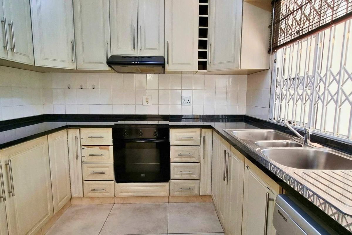 Functional kitchen featuring built-in cabinetry, granite countertops, a double basin sink, and integrated oven with extractor fan, finished with a tiled backsplash.