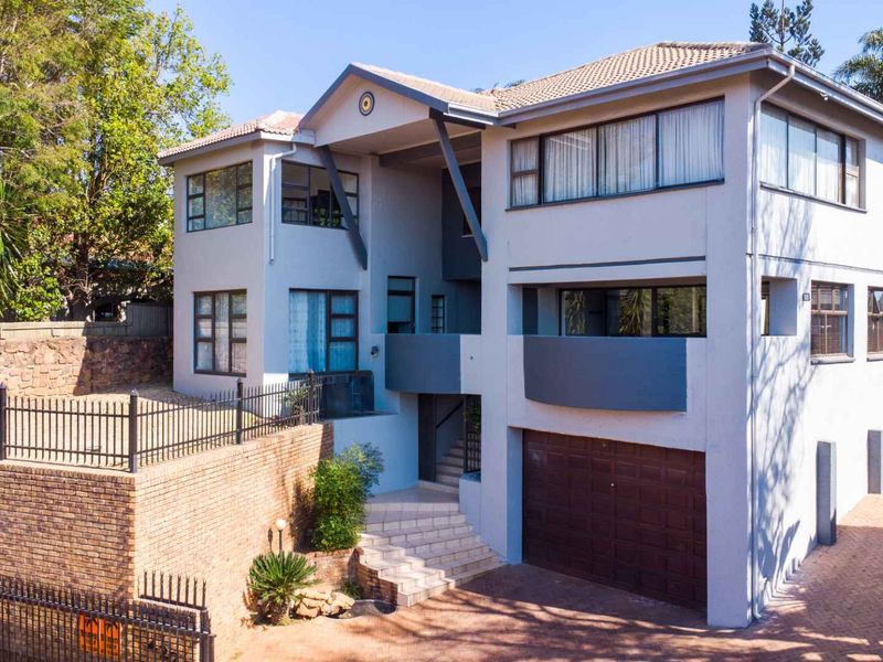 A multi-level residential property featuring a paved driveway, integrated garage, and elevated entrance with brick retaining walls and secure perimeter fencing.