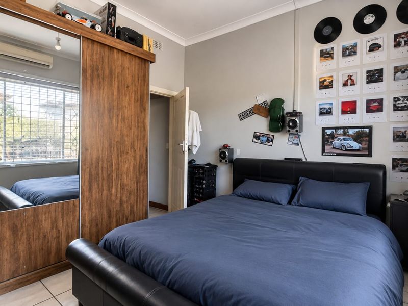A well-maintained bedroom featuring tiled flooring, a large built-in wardrobe with mirrored sliding doors, and a wall-mounted split-system air conditioner.