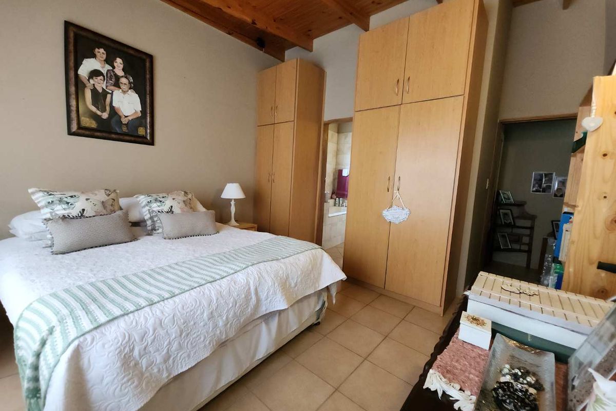 A bedroom featuring high vaulted timber ceilings, built-in wooden cabinetry, and tiled flooring, with an adjoining en-suite bathroom visible.