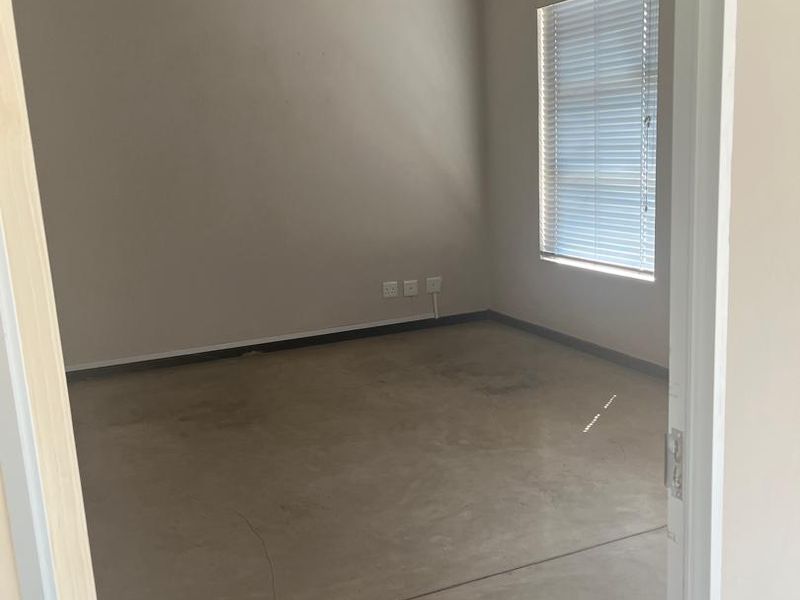 An empty office space featuring polished concrete floors, an exposed concrete ceiling, a wall-mounted air conditioner, and large windows with fitted blinds.