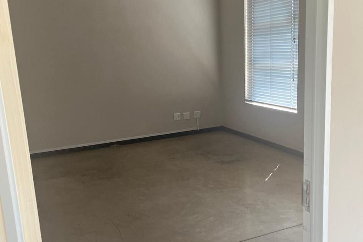 An empty office space featuring polished concrete floors, an exposed concrete ceiling, a wall-mounted air conditioner, and large windows with fitted blinds.