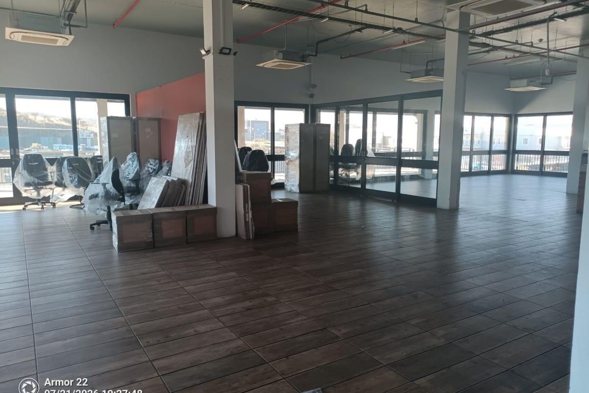 Spacious open-plan retail or office area featuring wood-look tiled flooring, exposed industrial-style ceilings, and extensive glass partitioning for natural light.