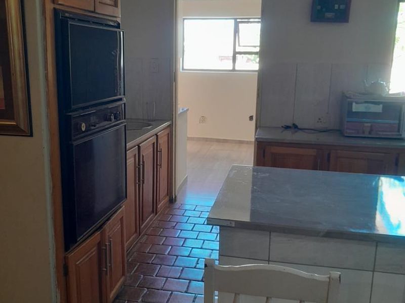A functional kitchen featuring wooden cabinetry, tiled countertops, a built-in oven, and a central island, with direct access to an adjacent room.