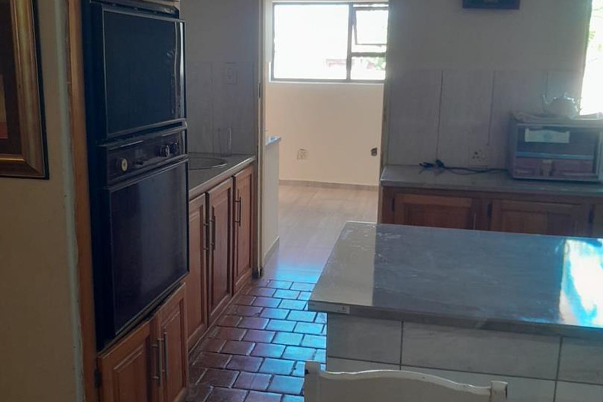 A functional kitchen featuring wooden cabinetry, tiled countertops, a built-in oven, and a central island, with direct access to an adjacent room.