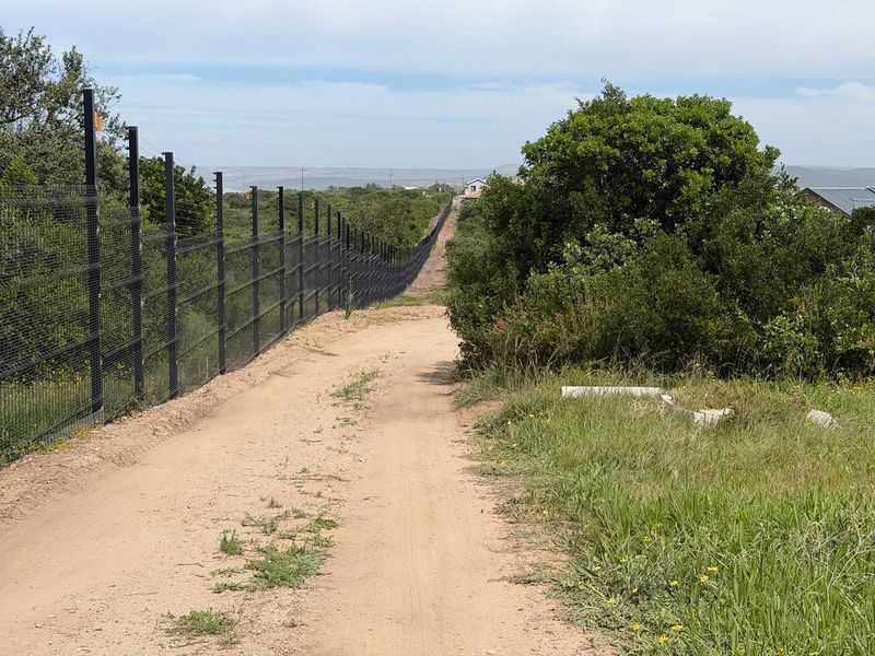 A view of a dirt access road running alongside a perimeter fence on a vacant residential plot.