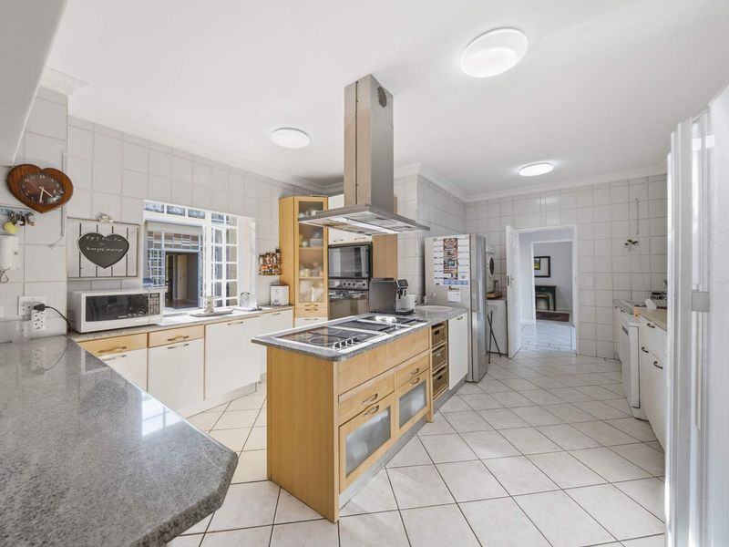 Spacious kitchen featuring a central island with a built-in hob, extractor fan, ample cabinetry, and tiled finishes throughout.