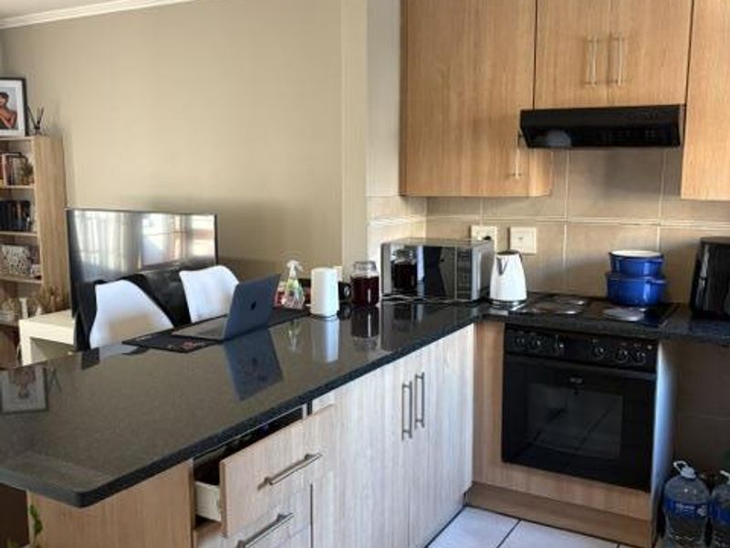 A functional kitchen featuring light wood cabinetry, a granite-topped island, built-in oven and hob, and tiled flooring, offering a practical layout for daily use.