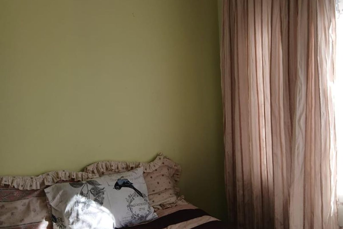A bedroom featuring light green walls and floor-to-ceiling curtains, providing a simple and functional sleeping space.