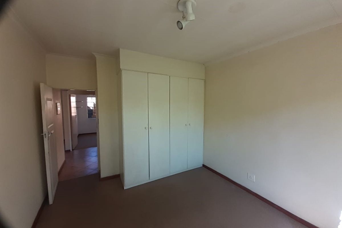 An empty bedroom featuring built-in cupboards, carpeted flooring, and a ceiling light fixture, offering a blank canvas for personalization.