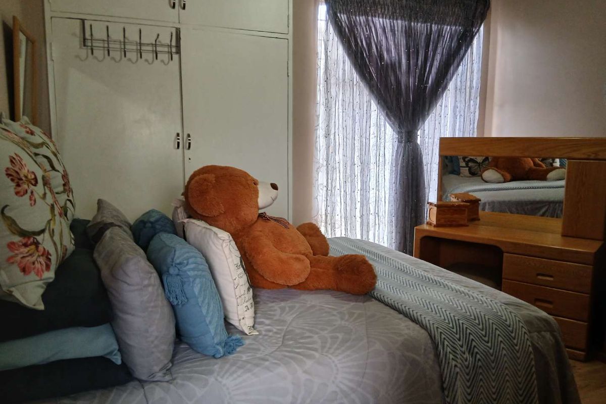 A bedroom featuring built-in cupboards and a window with sheer curtains, providing a functional and lived-in space.