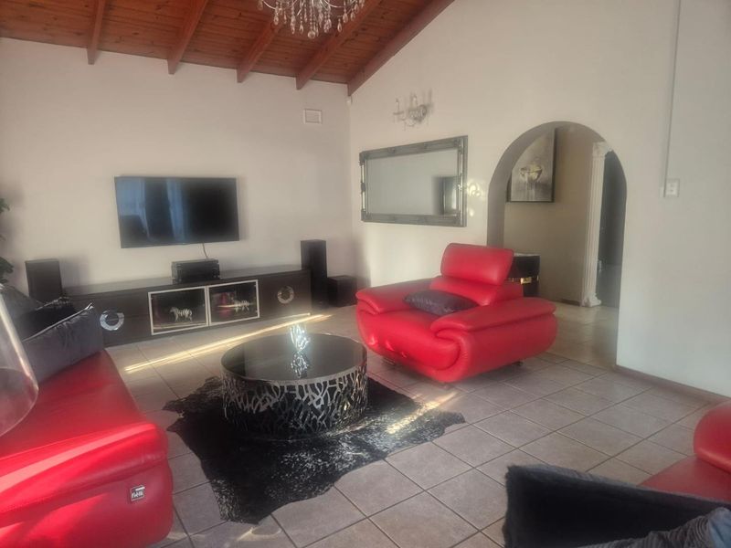 Spacious living room featuring a high exposed timber beam ceiling, ceramic tiled flooring, and an elegant arched doorway leading to adjacent areas.