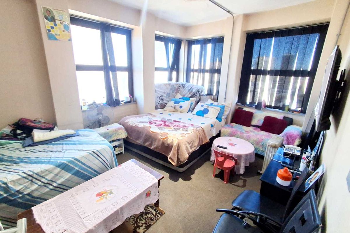 A bedroom featuring large windows providing natural light, with visible exposed electrical conduit and signs of wear on the ceiling and flooring.