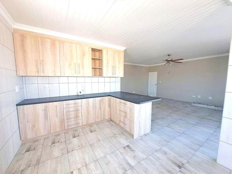 An open-plan kitchen and living area featuring modern light wood cabinetry, dark countertops, tiled flooring, and a ceiling fan.