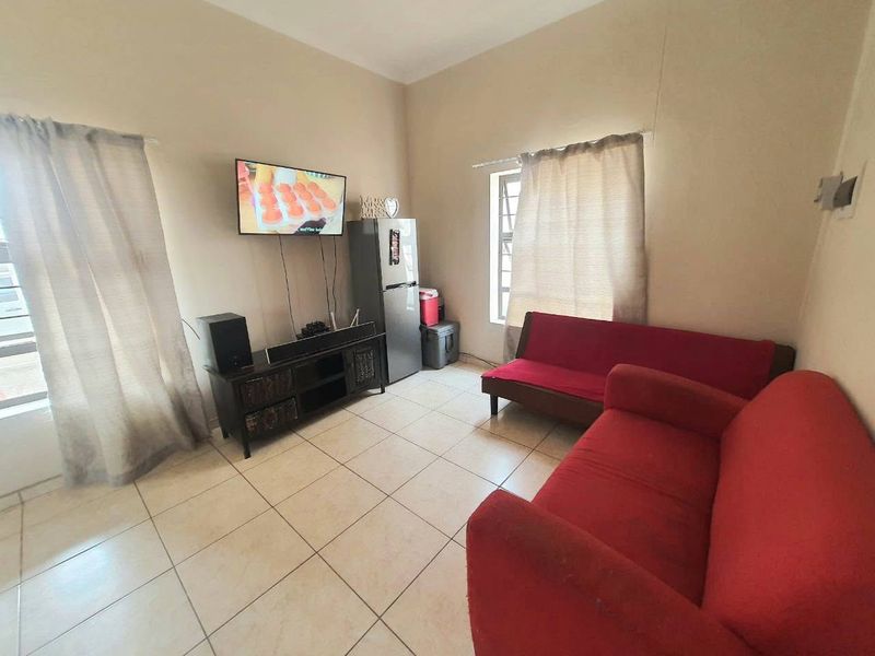 A functional living room featuring tiled flooring and natural light through multiple windows, providing a neutral base for potential interior updates.
