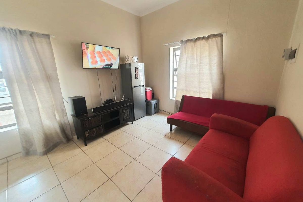 A functional living room featuring tiled flooring and natural light through multiple windows, providing a neutral base for potential interior updates.