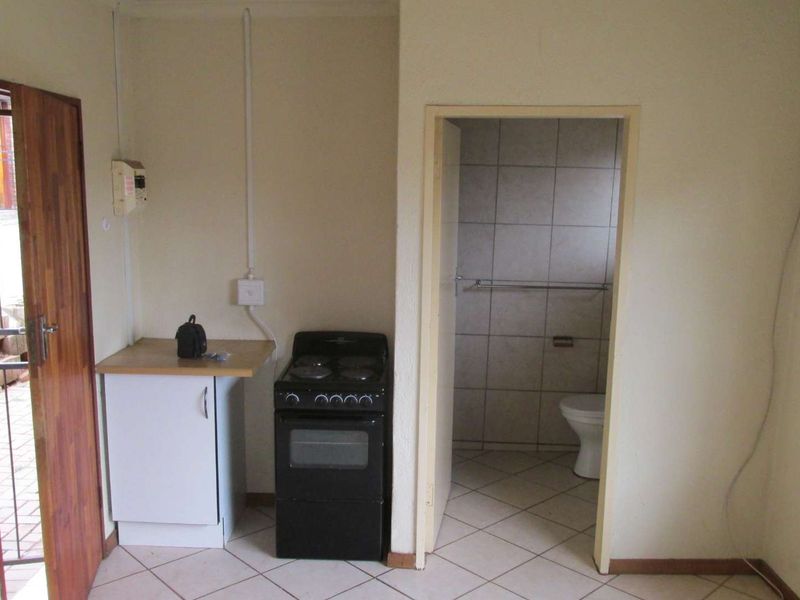 A compact kitchen area featuring a freestanding stove, base cabinetry, and direct access to an adjacent tiled bathroom.