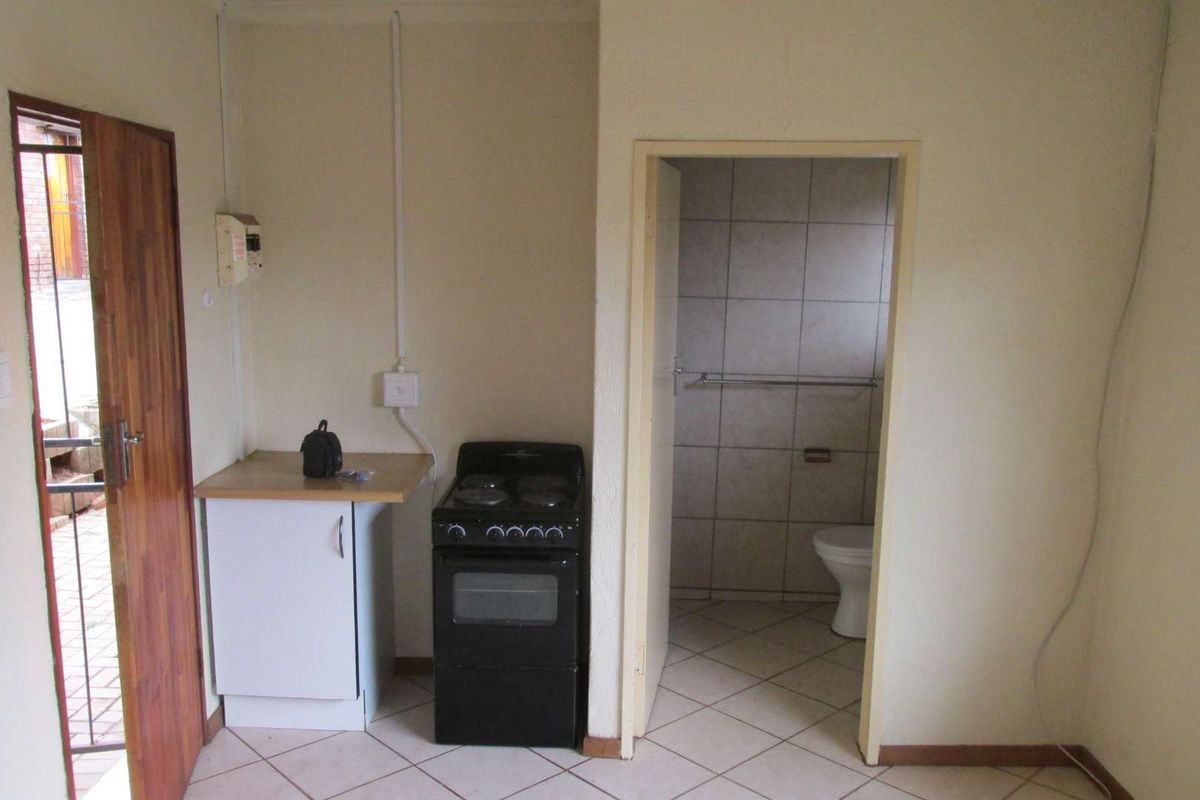 A compact kitchen area featuring a freestanding stove, base cabinetry, and direct access to an adjacent tiled bathroom.