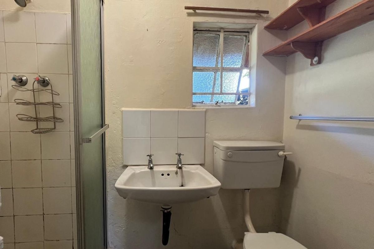 A compact, dated bathroom featuring a shower enclosure, wall-mounted basin, and toilet, requiring cosmetic updates and modernization of fixtures.