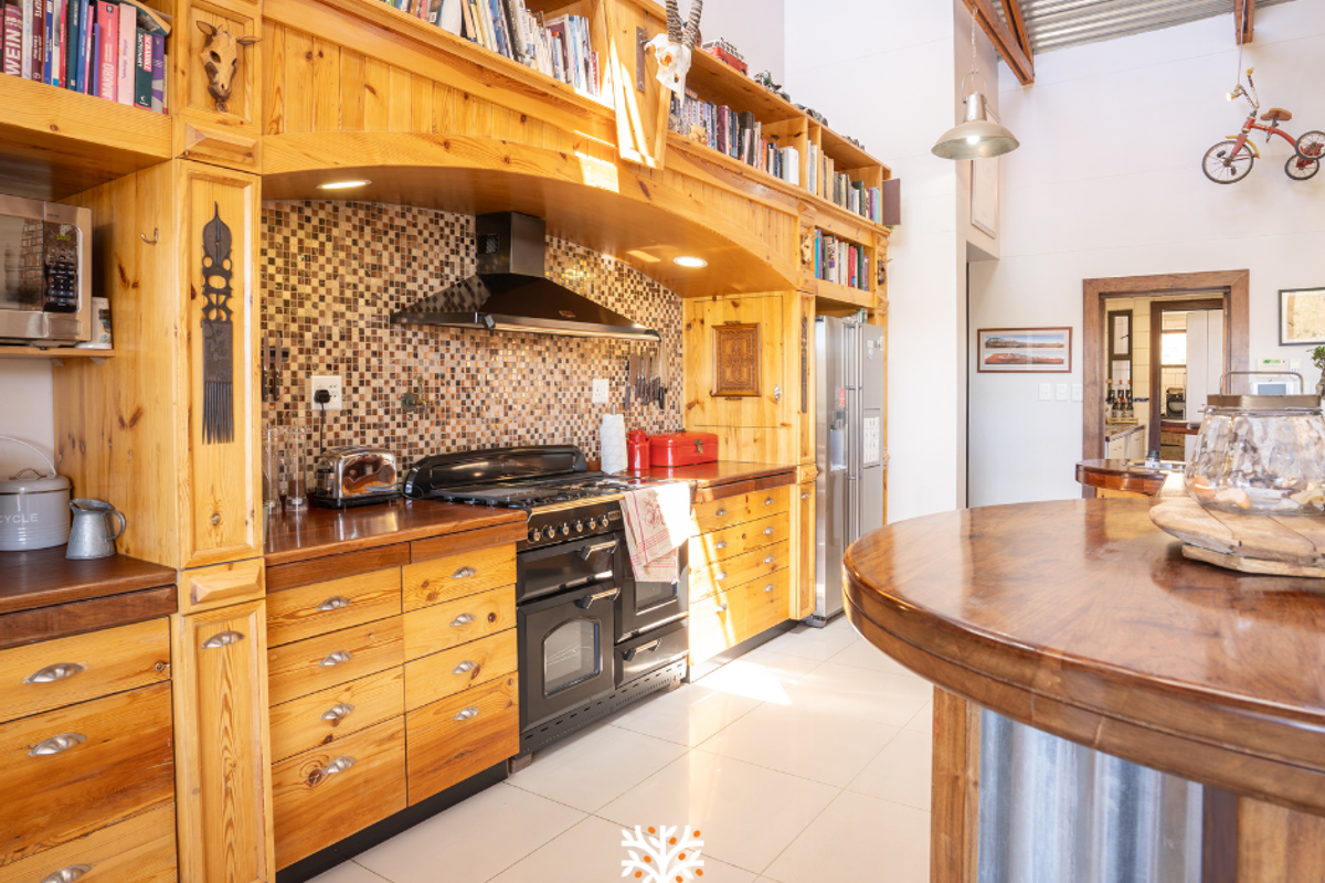 A rustic-style kitchen featuring extensive custom timber cabinetry, a mosaic tile backsplash, a black range cooker with extractor fan, and a large wooden breakfast bar.