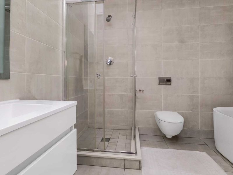 Modern bathroom featuring a walk-in shower, wall-hung toilet, freestanding bathtub, and a sleek vanity cabinet with neutral floor-to-ceiling tiling.