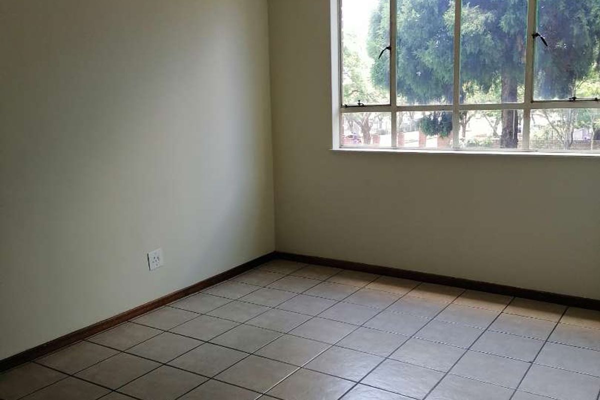 A bright, empty living area featuring large windows, neutral walls, and tiled flooring, offering a versatile space ready for personalization.