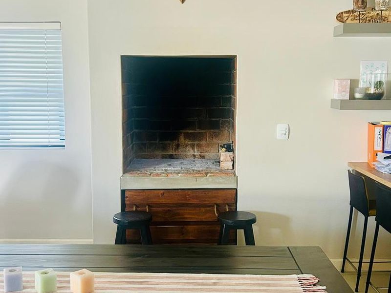 A living area featuring a built-in brick fireplace, floating wall shelves, and venetian blinds, providing a cozy and functional space.