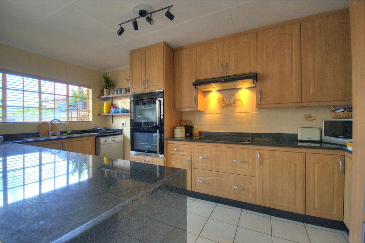 A functional kitchen featuring light wood cabinetry, dark granite countertops, a built-in oven, and an integrated extractor fan with tiled flooring.