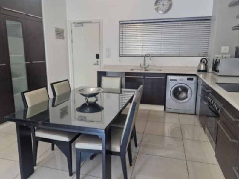 Open-plan kitchen and dining area featuring dark wood cabinetry, integrated appliances, tiled flooring, and a functional layout suitable for modern apartment living.