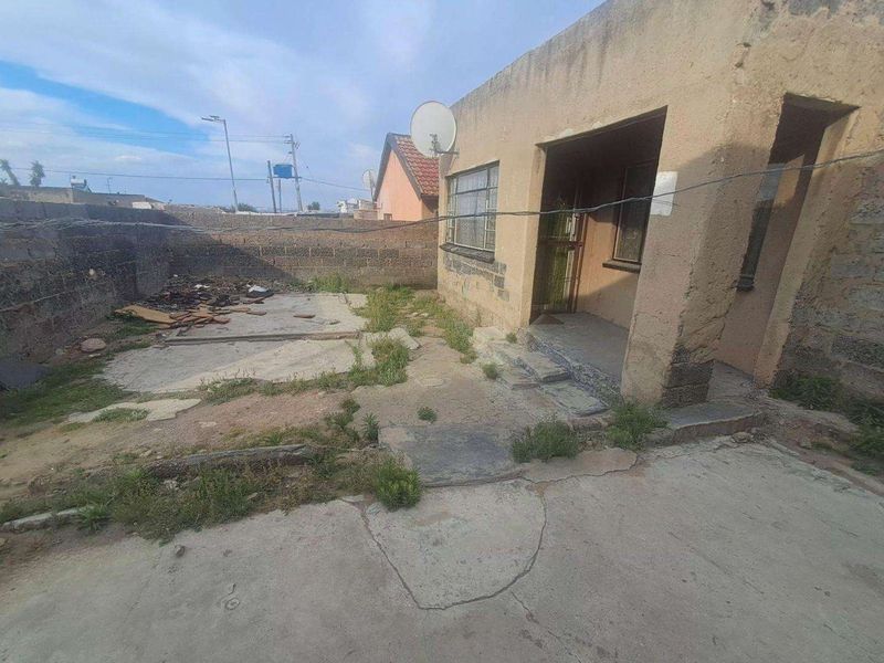 Rear exterior view of the property featuring a concrete patio area, perimeter boundary wall, and weathered building facade requiring maintenance.